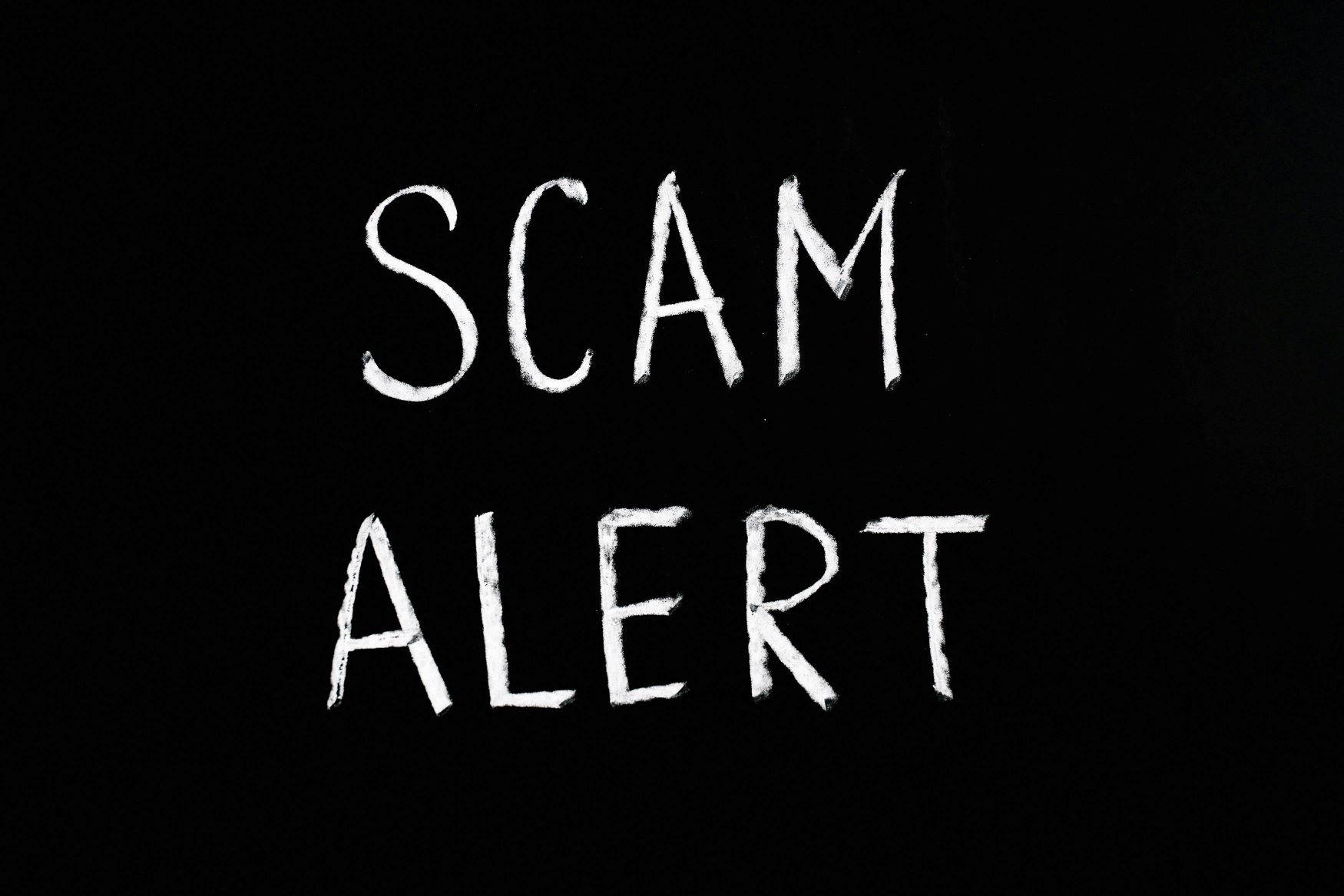 The words 'Scam Alert' written in white chalk on blackboard.